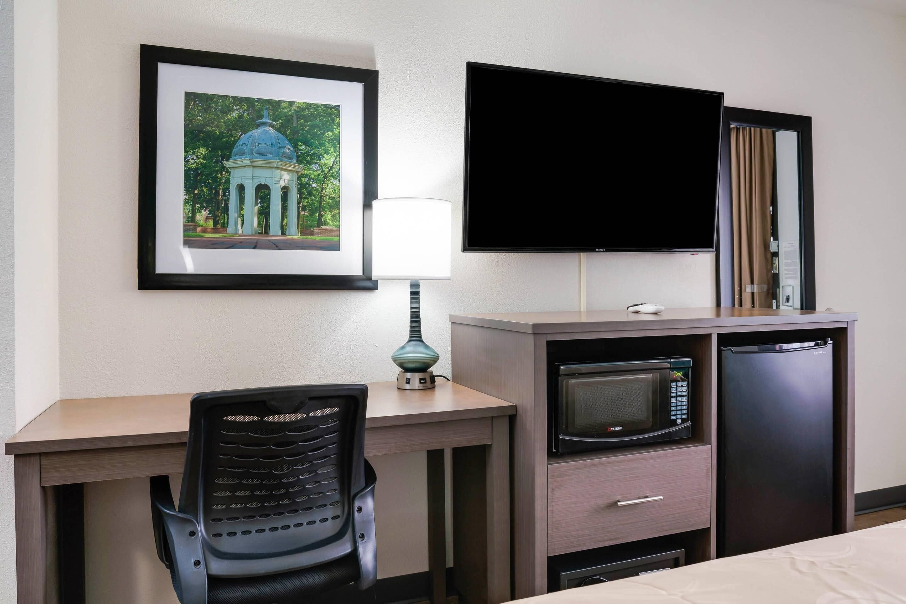 Habitación de hotel con escritorio, silla, televisor, microondas y refrigerador.