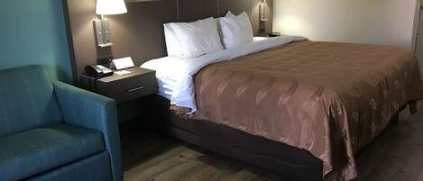 Una habitación de hotel con cama, dos mesitas de noche, un escritorio con teléfono, una silla y dos lámparas de pared.