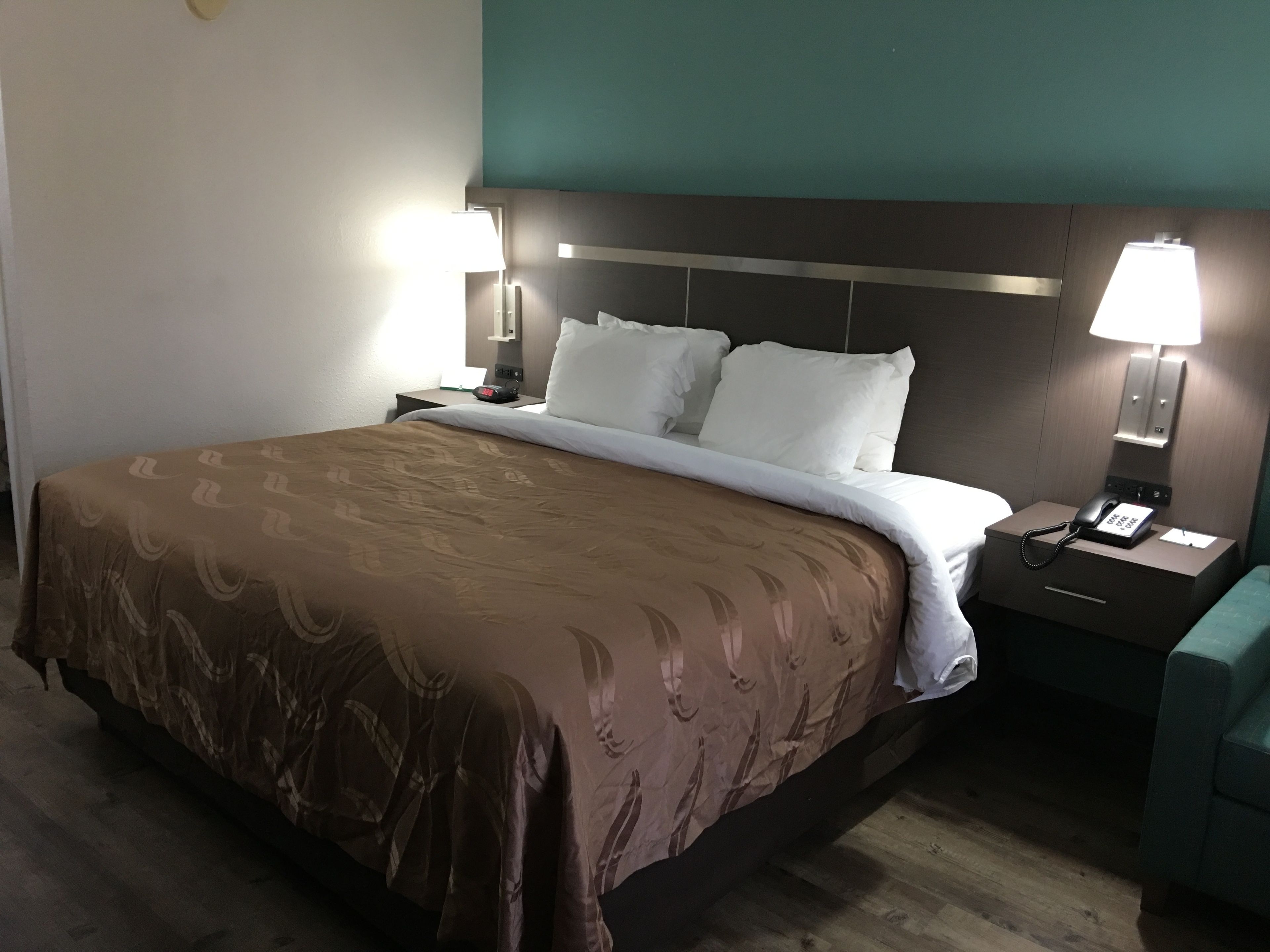 A hotel room with a large bed, two bedside tables, a nightstand, a lamp, and a telephone.