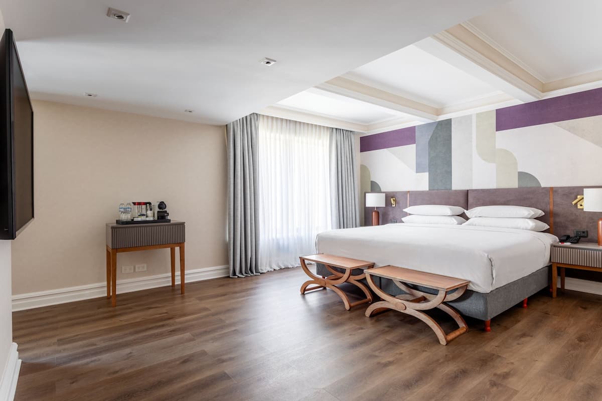 A hotel room with a large bed, bedside tables, a TV, and a window with curtains.