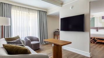 Een moderne hotelkamer met een bank, fauteuil, televisie en houten vloer.