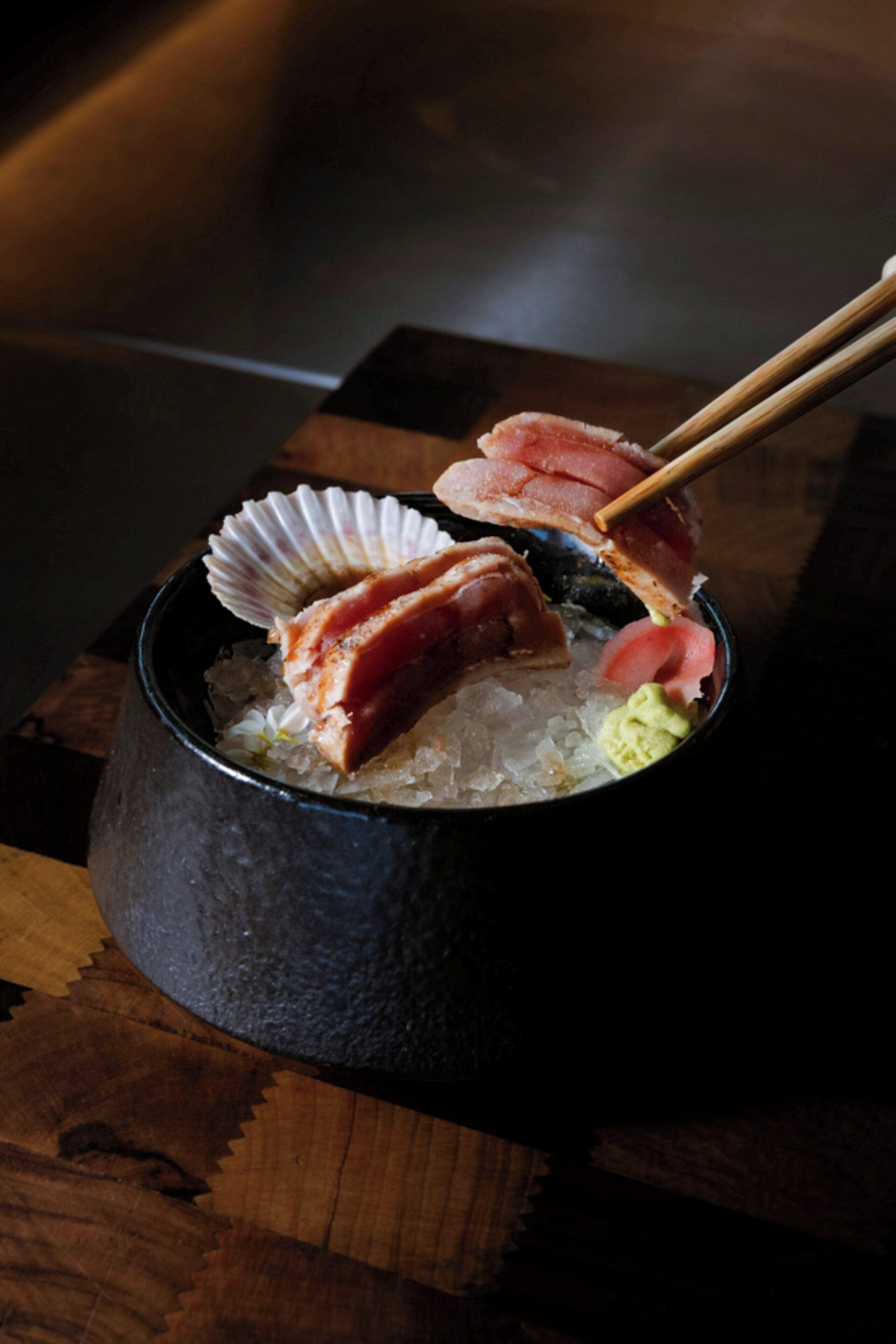 Un bol de sushis, avec des baguettes soulevant un morceau de poisson.