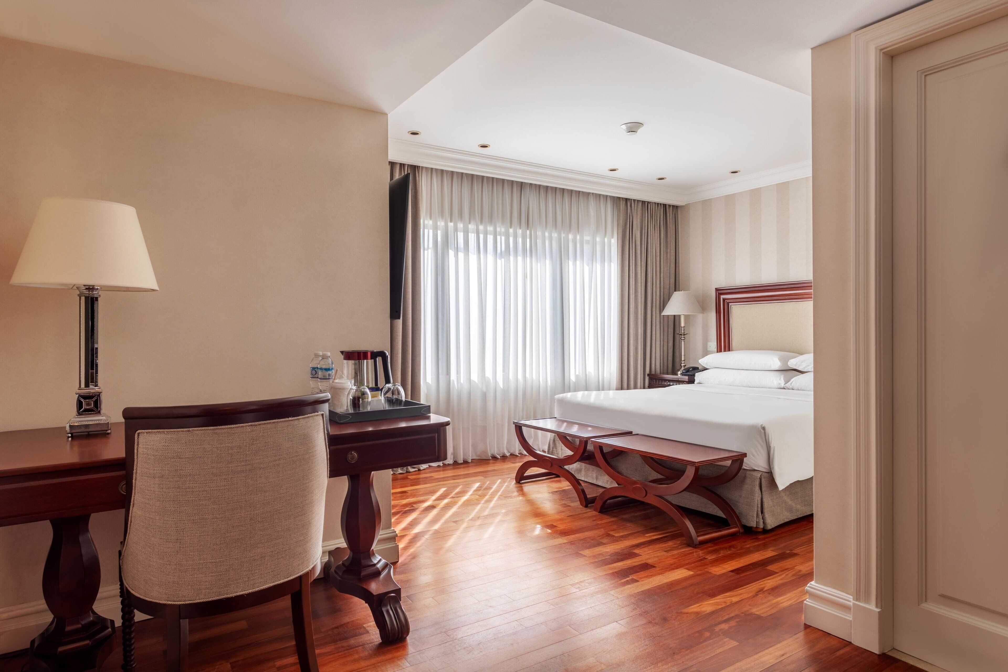 Ein Hotelzimmer mit einem Holztisch, einem Stuhl, einem Bett und einem großen Fenster mit Vorhängen.