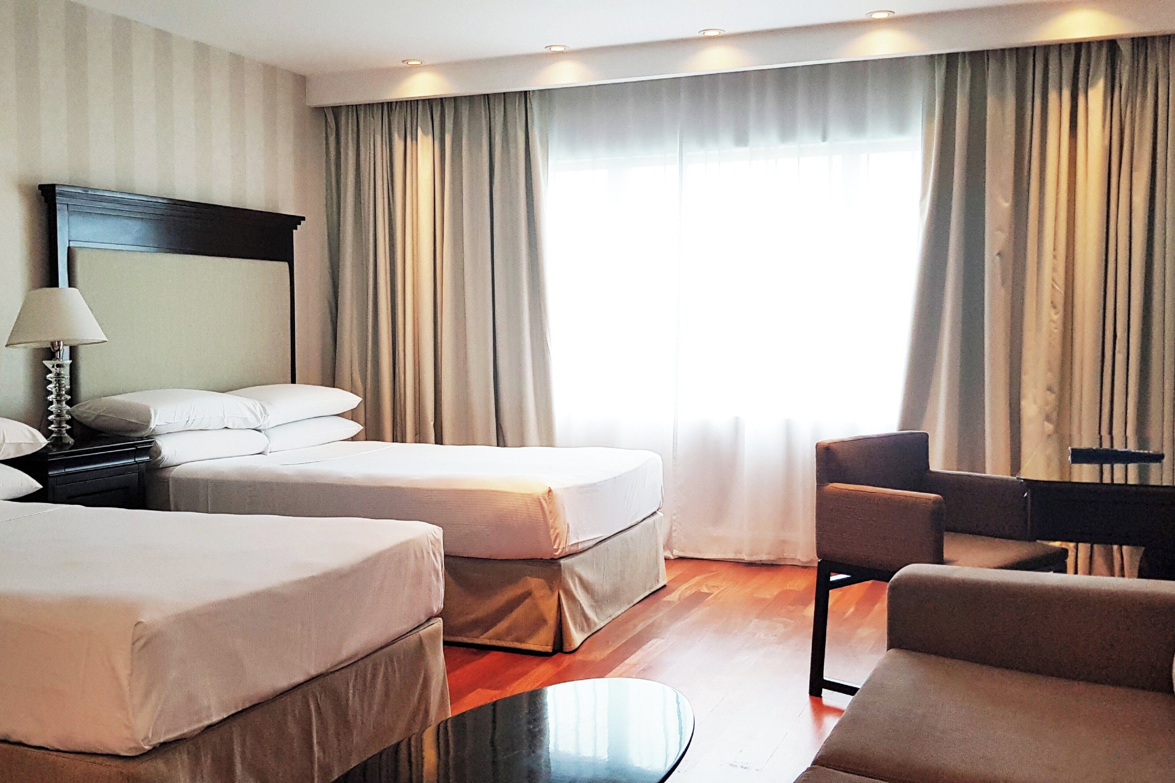 Een hotelkamer met twee bedden, een bureau, een stoel en een groot raam met gordijnen.