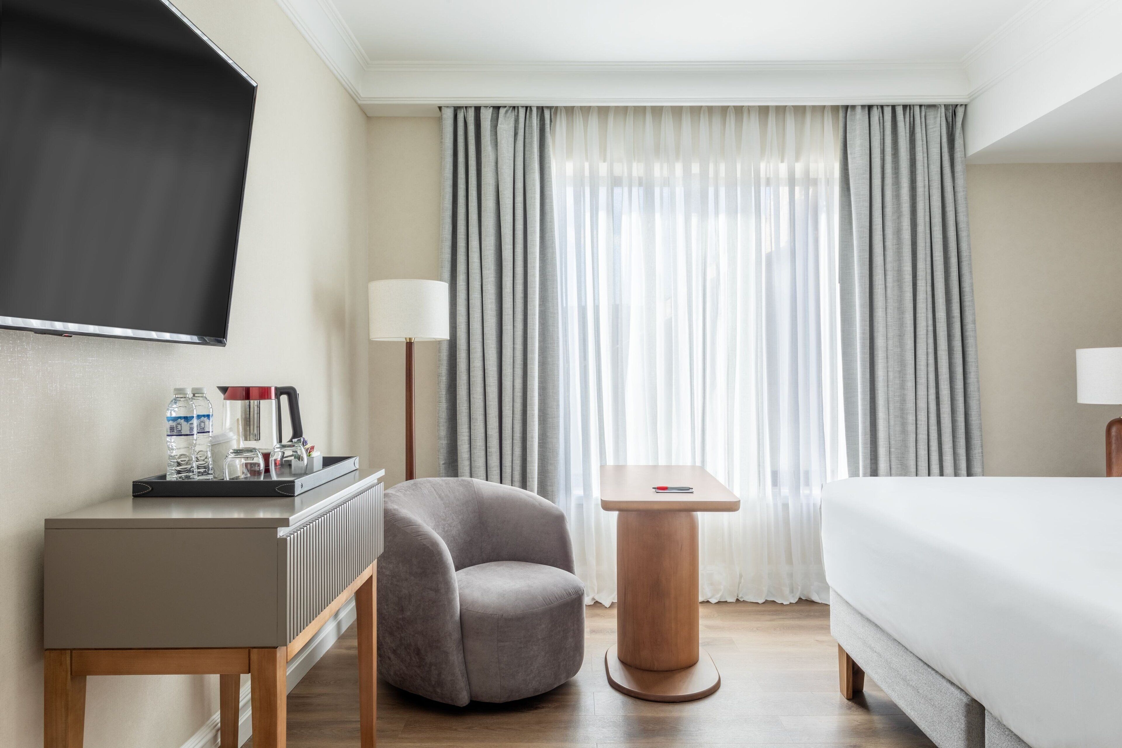 Una habitación de hotel con una cama, un escritorio con una silla, un televisor y una ventana con cortinas.