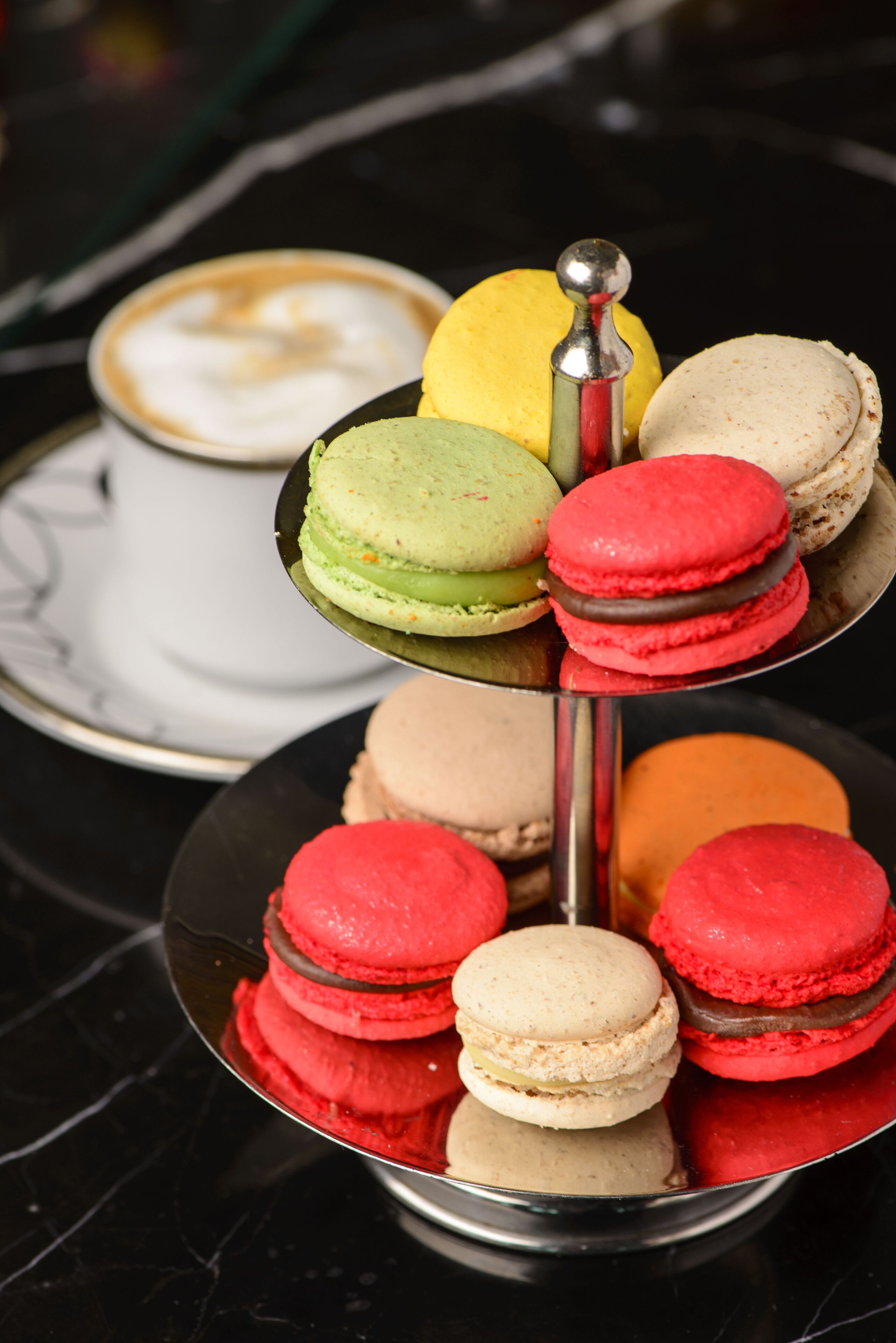 Un aparador en terrasses amb diversos macarrons de diferents colors i una tassa de cafè.