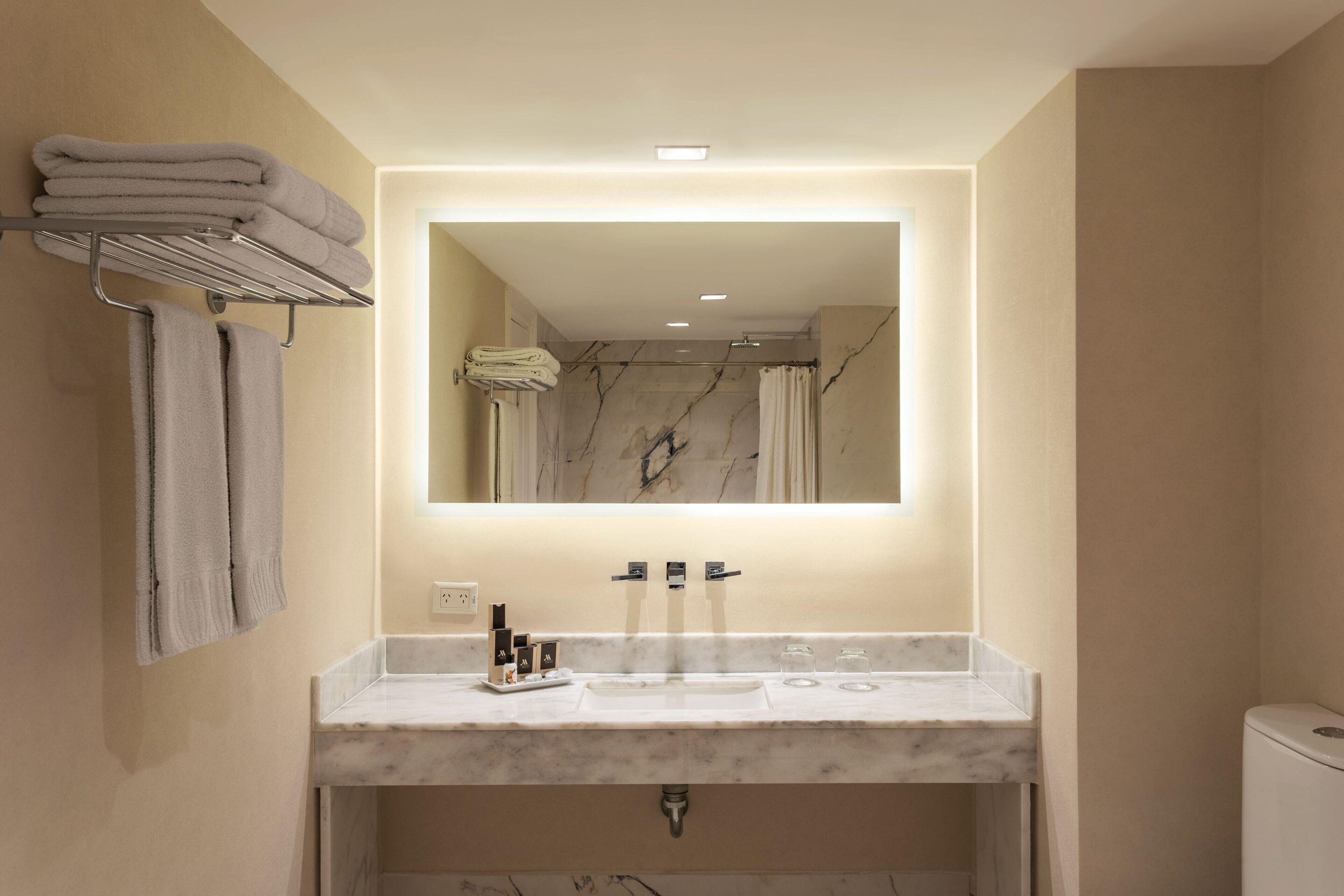 Un baño moderno con un lavabo de mármol, un espejo grande y un perchero para toallas.
