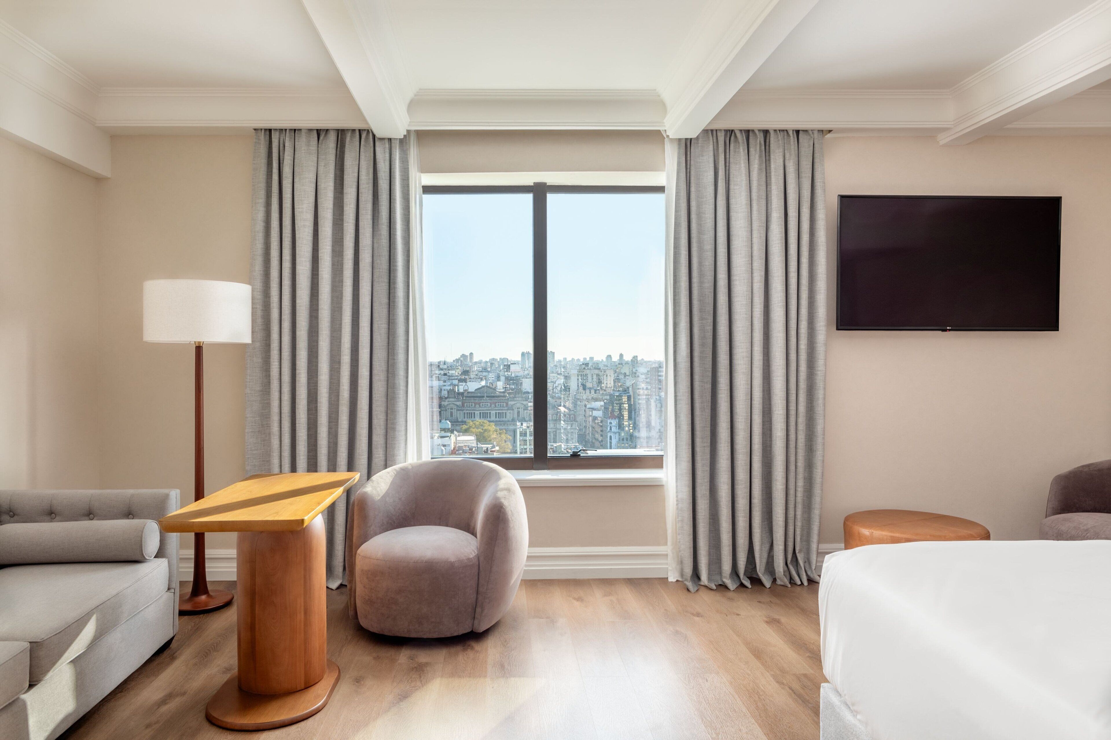 Een hotelkamer met uitzicht op de stad, een flatscreen televisie, een bank, een stoel, een houten bijzettafeltje en een bed.