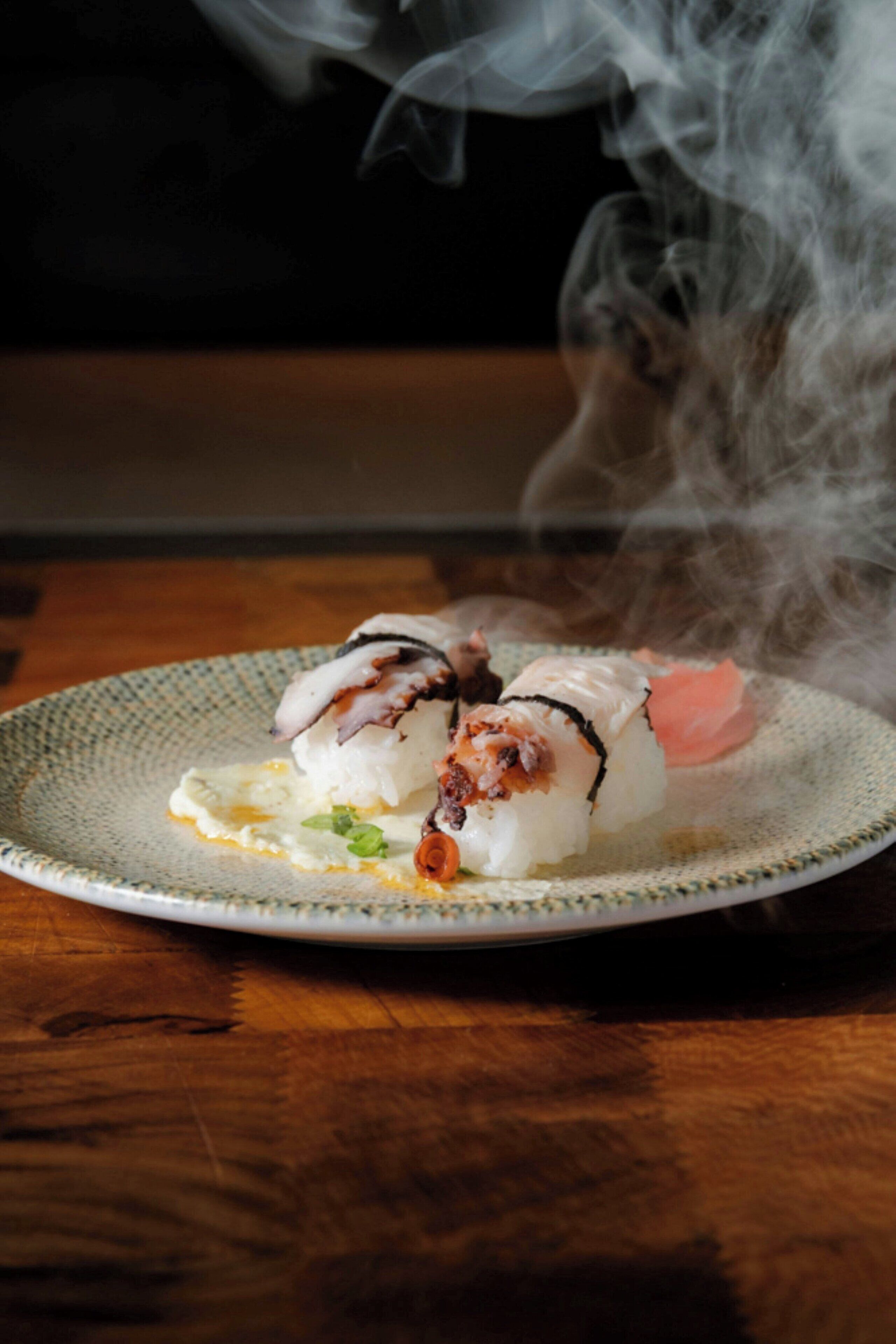 A plate of sushi with a decorative plate and smoke rising from the food.
