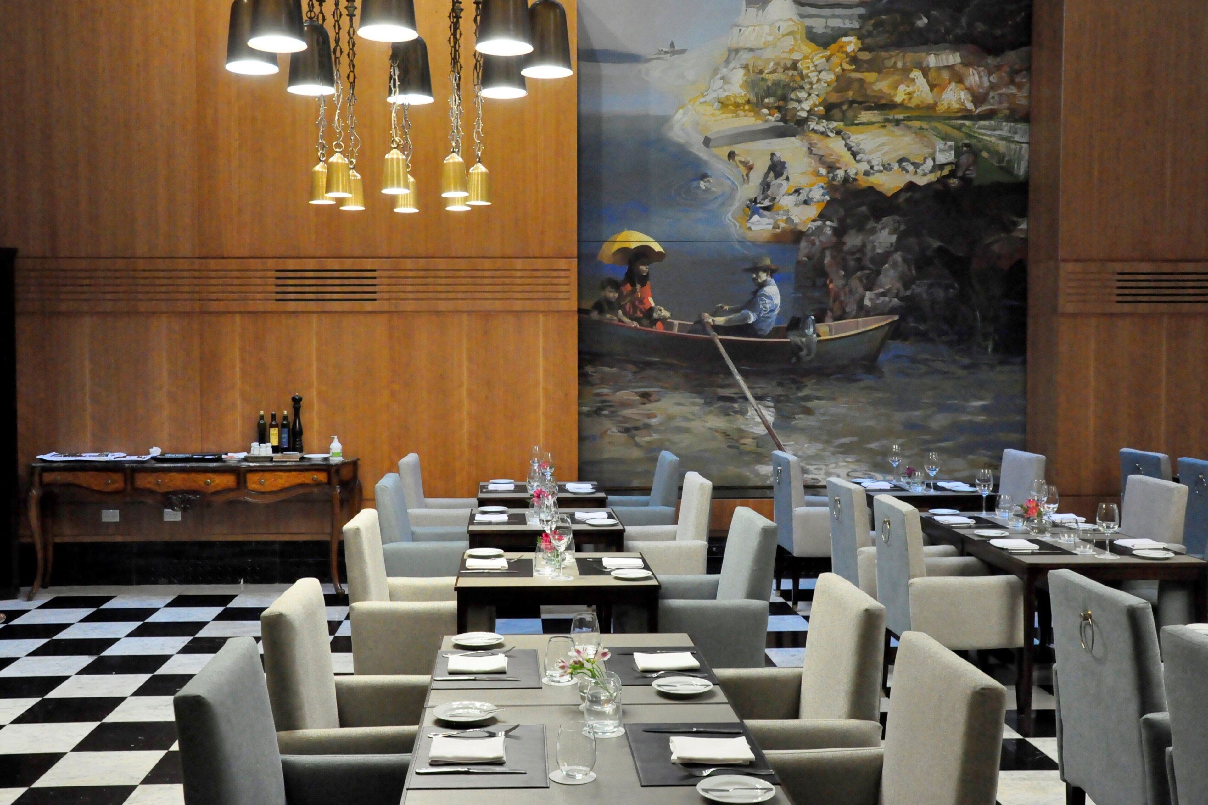A restaurant with a checkered floor, tables set with plates and glasses, and a mural of a river scene on the wall.