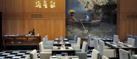 A restaurant with a checkered floor, tables set with plates and glasses, and a mural of a river scene on the wall.