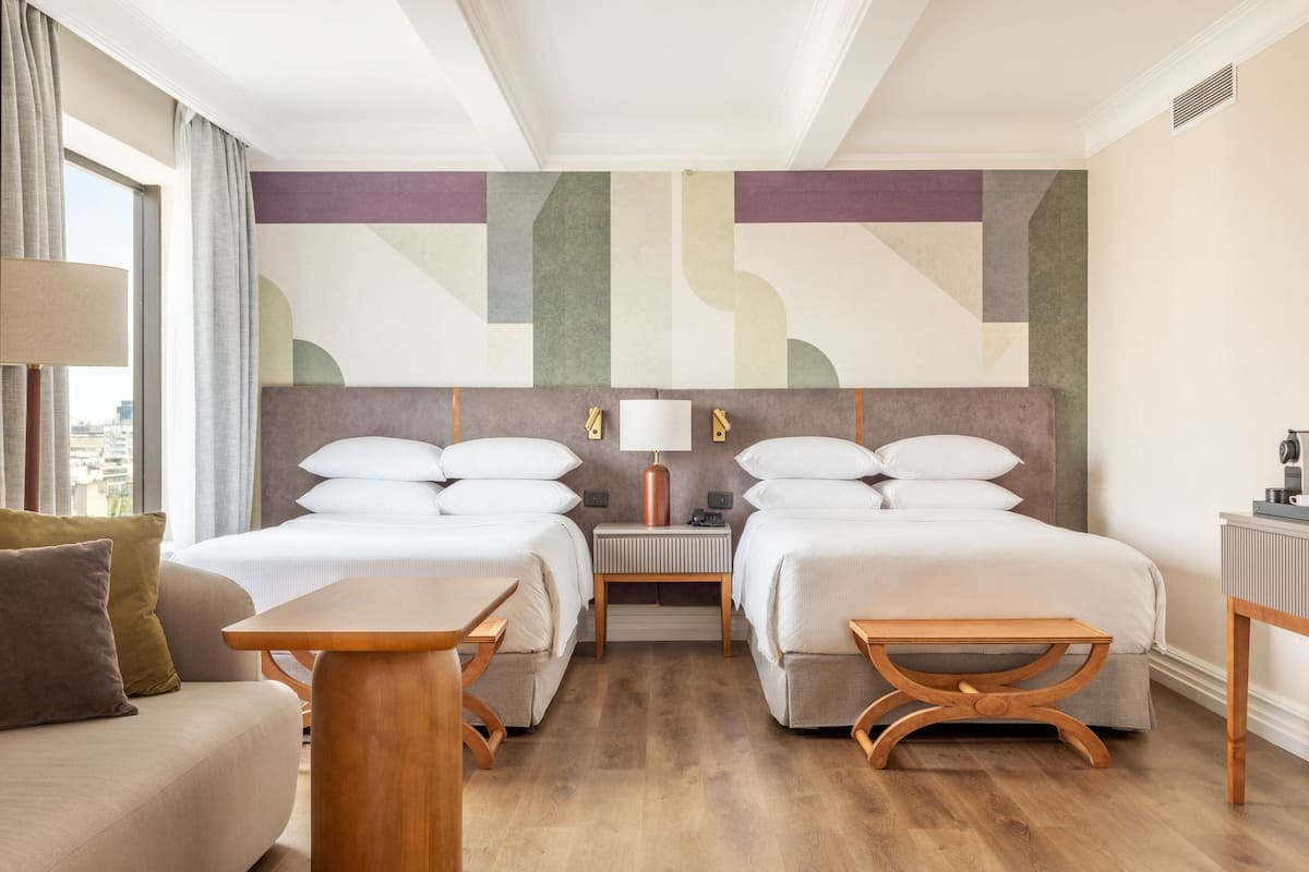 A hotel room with two beds, a sofa, a table, and a lamp.