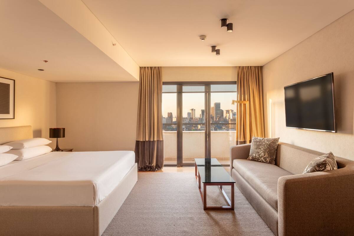 A hotel room with a large bed, a sofa, a small table, and a TV.