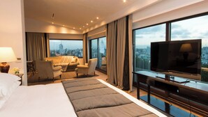 Una camera d'hotel moderna con un letto grande, una TV, un angolo salotto con vista sulla città e un'ampia finestra.