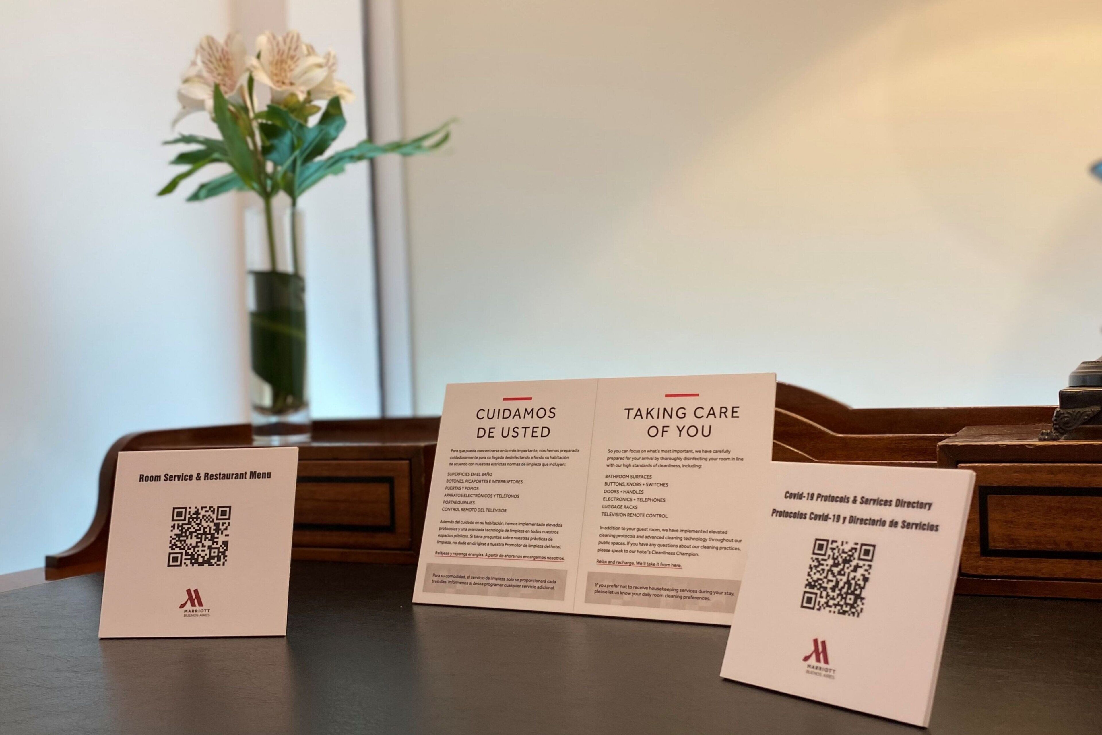 Ein Tisch mit drei Informationskarten, davon eine mit der Aufschrift „Zimmerservice & Restaurantkarte“ und die anderen beiden mit „Wir kümmern uns um Sie“ und „Für Ihr Wohlbefinden“, jede mit einem QR-Code.