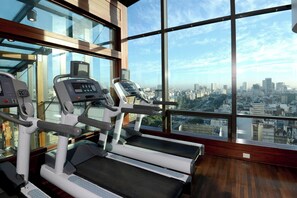 A gym with treadmills and exercise equipment, large windows with a city view.