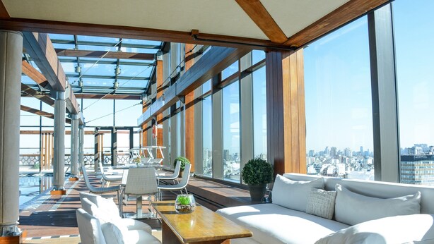 Un moderno lounge rooftop con vista sulla città, con divani, poltrone e zona pranzo.