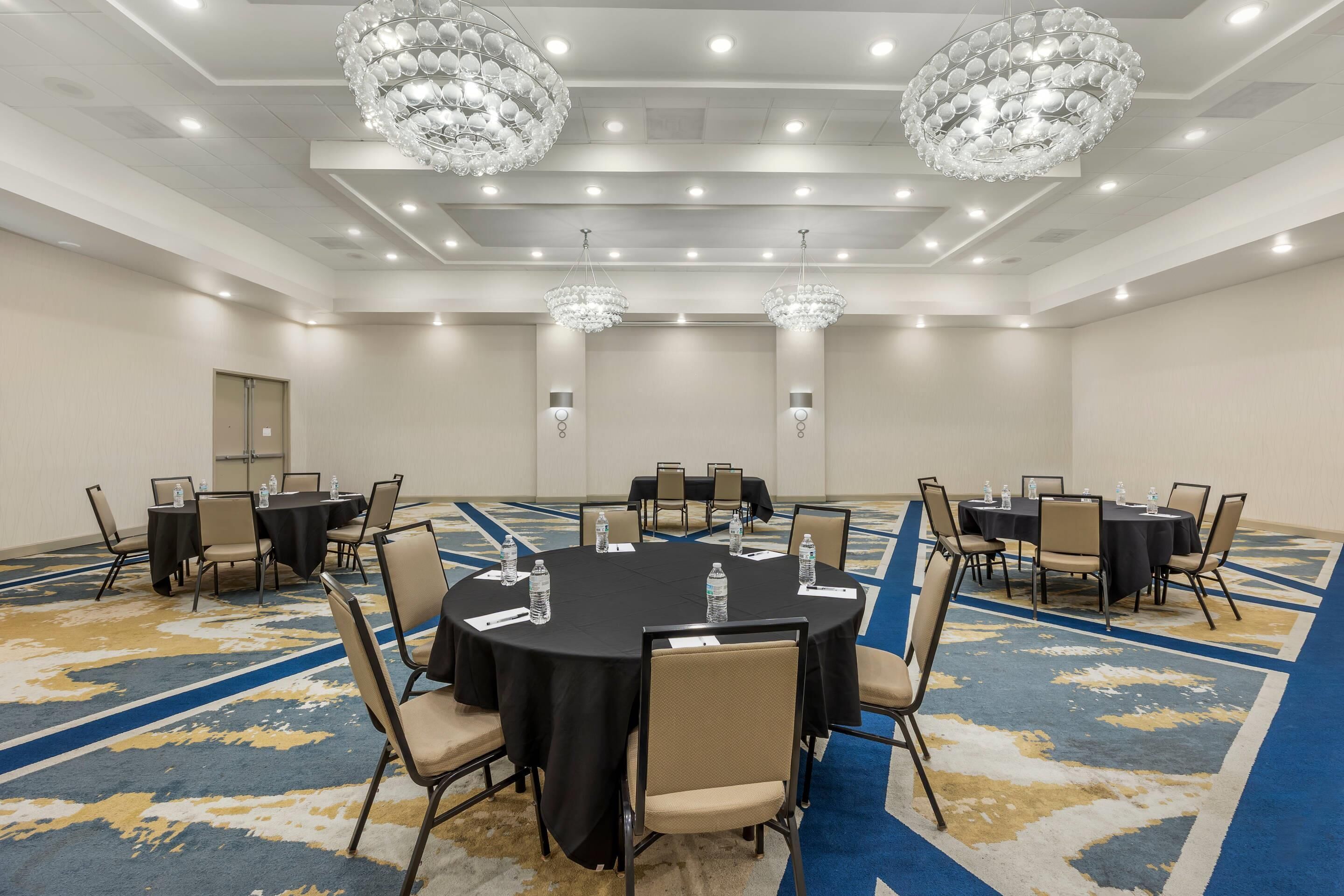 Une salle de conférence équipée de tables rondes, de chaises et de lustres.