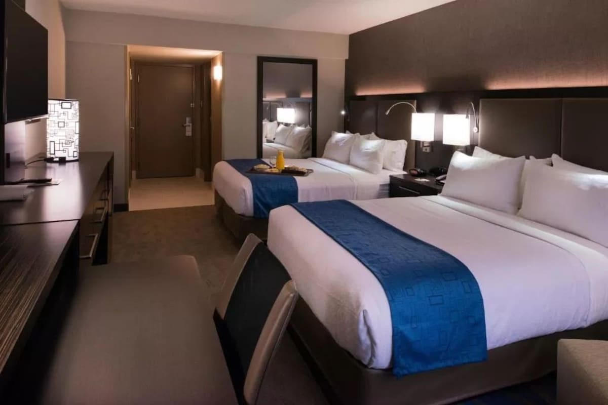 A hotel room with two beds, a desk, a TV, and a mirror.