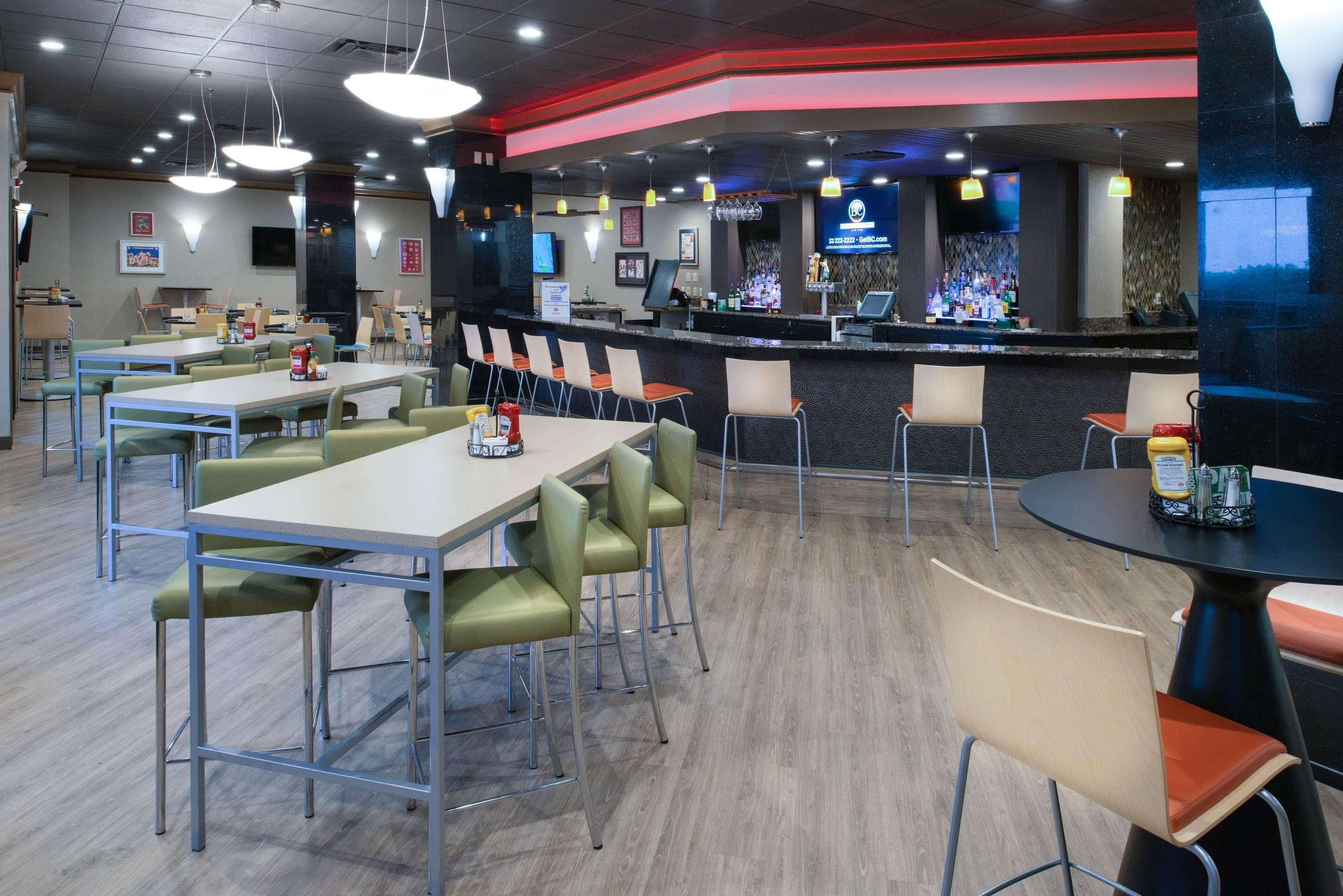 Un restaurante con varias mesas y sillas, una zona de bar con mostrador, y una pantalla de televisión.