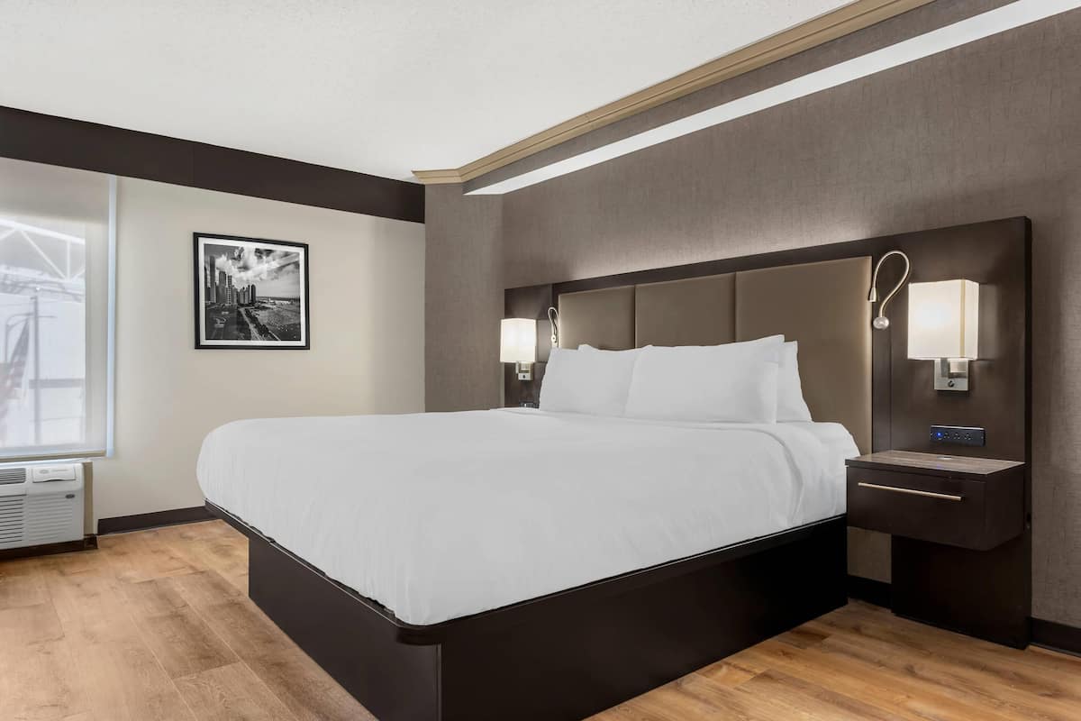 A modern hotel room with a large bed, bedside lamps, a nightstand, and a framed picture on the wall.