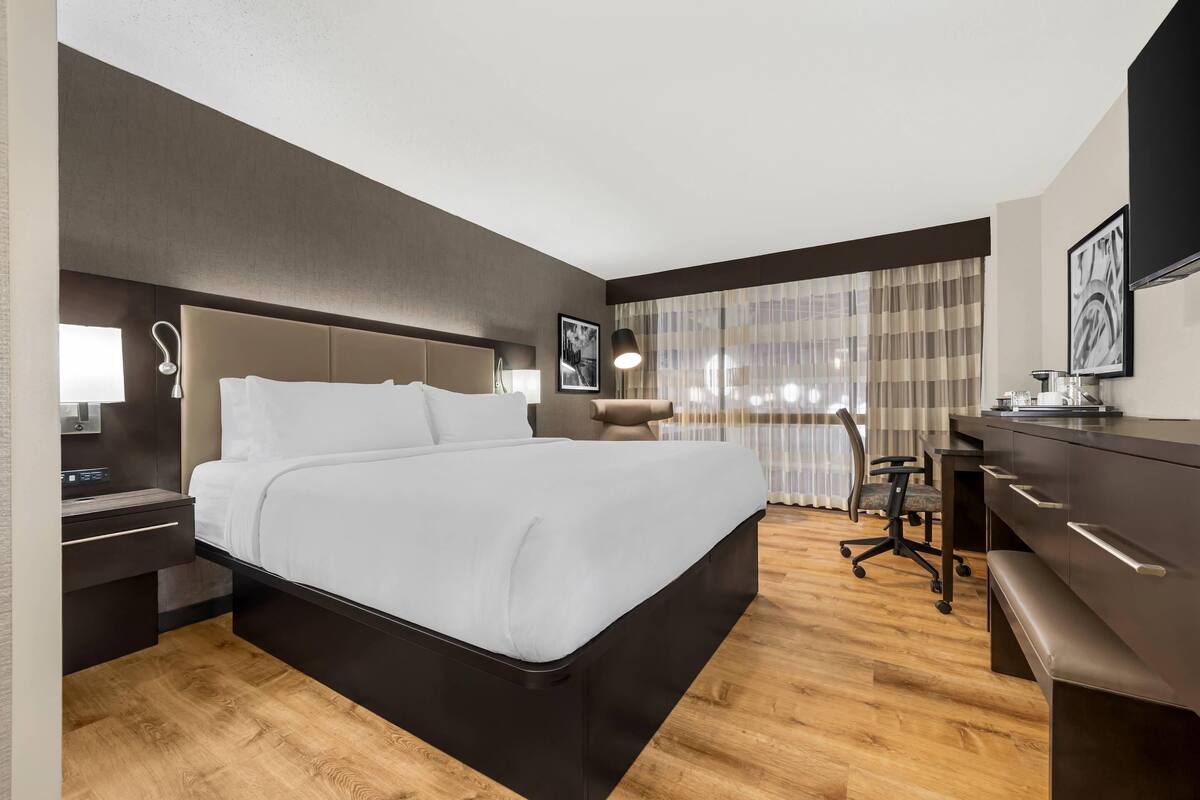 A hotel room with a large bed, a desk, a chair, and a window with curtains.