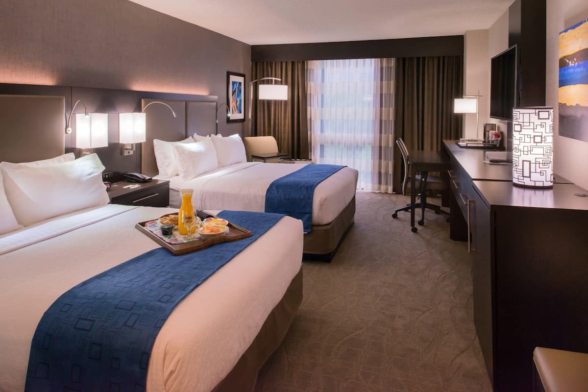 A hotel room with two beds, a desk, a chair, a TV, and a minibar.