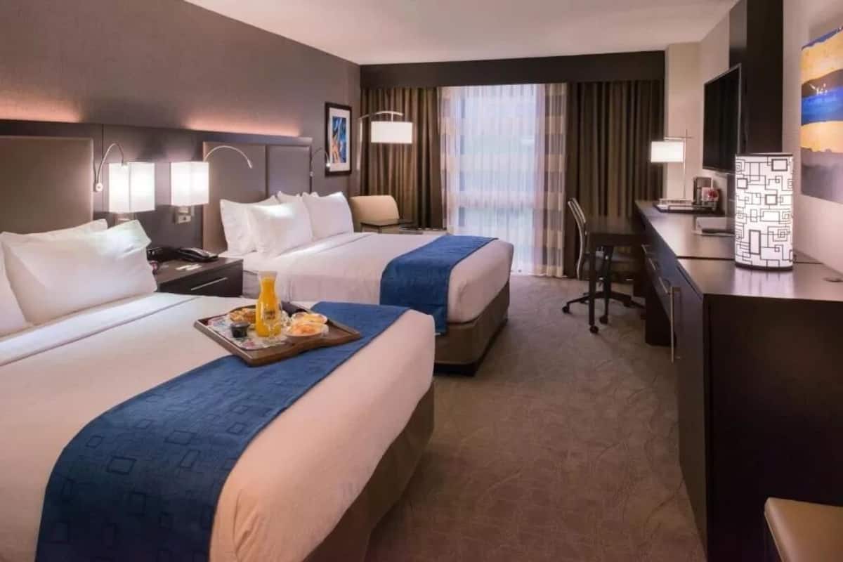A hotel room with two beds, a desk, a chair, a TV, and a minibar.