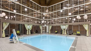 Une piscine intérieure dotée d’un haut plafond, de grandes fenêtres et de chaises longues.
