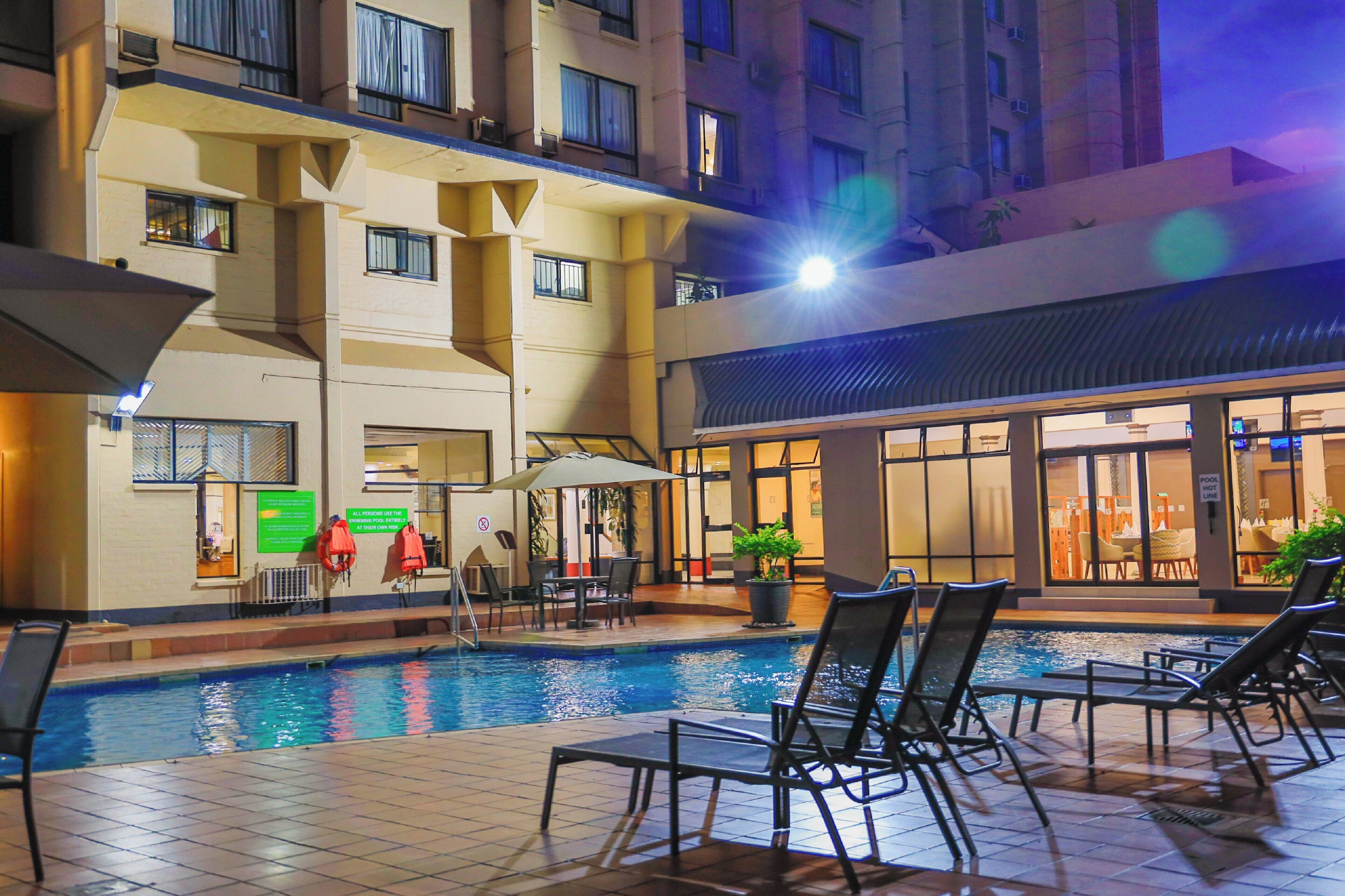 An indoor swimming pool with lounge chairs and a sunken seating area, surrounded by a building with multiple floors and balconies.
