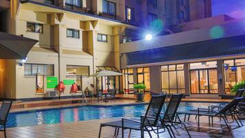An indoor swimming pool with lounge chairs and a sunken seating area, surrounded by a building with multiple floors and balconies.