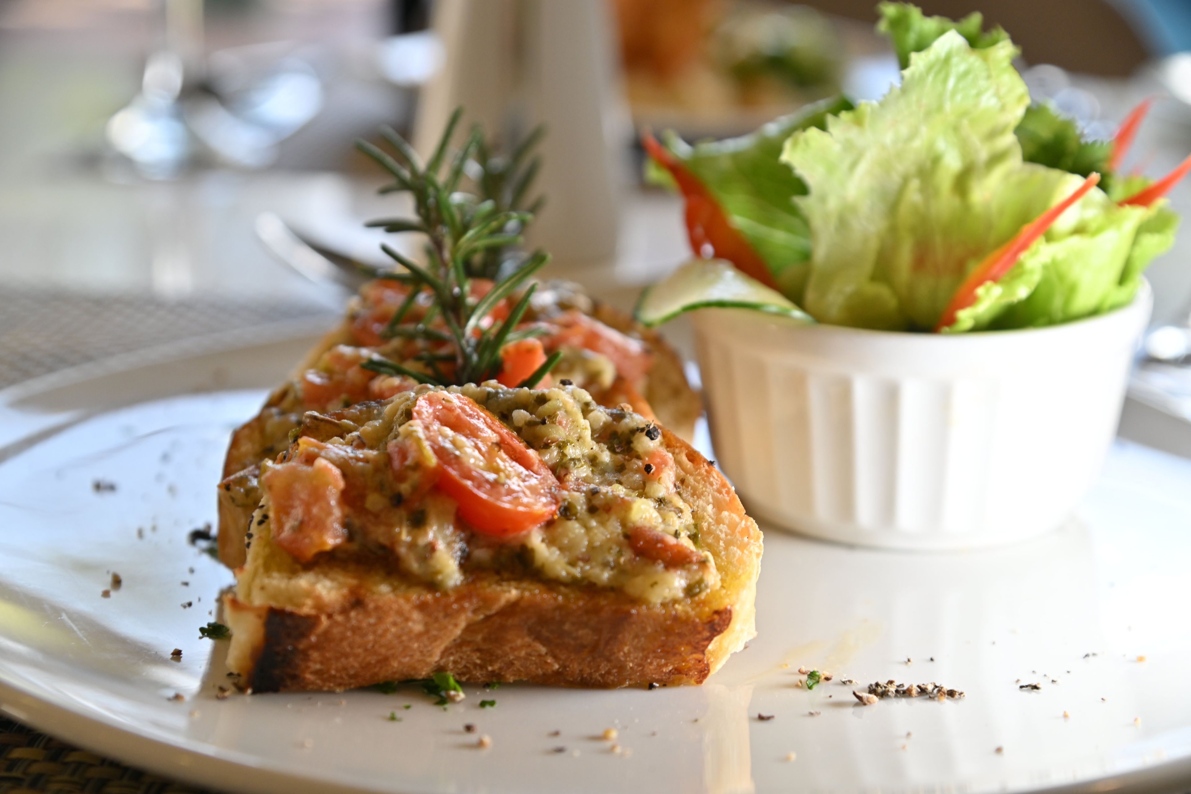 A slice of toasted bread topped with vegetables and herbs, accompanied by a side salad in a white bowl.