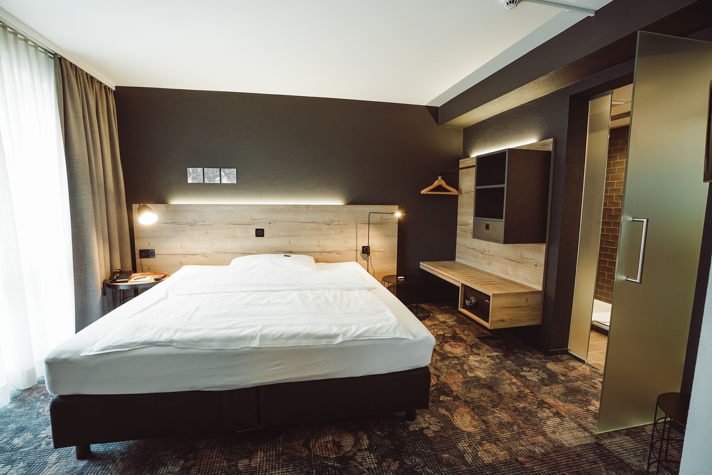 Habitació d'hotel moderna amb un llit gran, taules de nit, un mirall i una panxa de fusta.