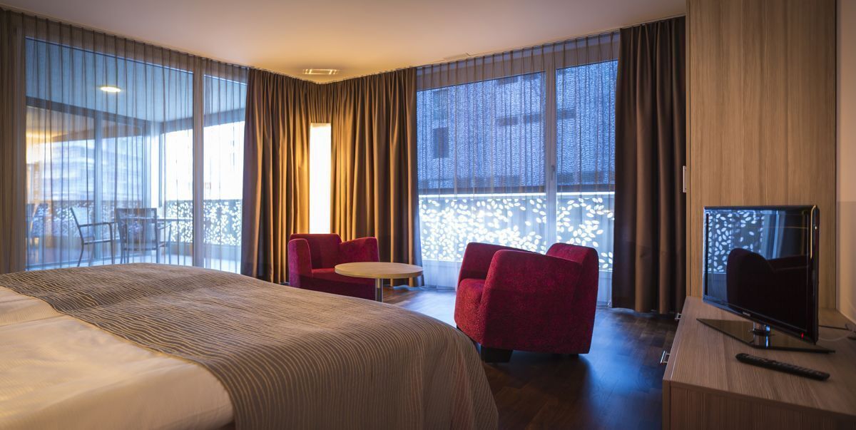 Una habitación de hotel con una cama grande, televisión, escritorio y balcón con sillas.