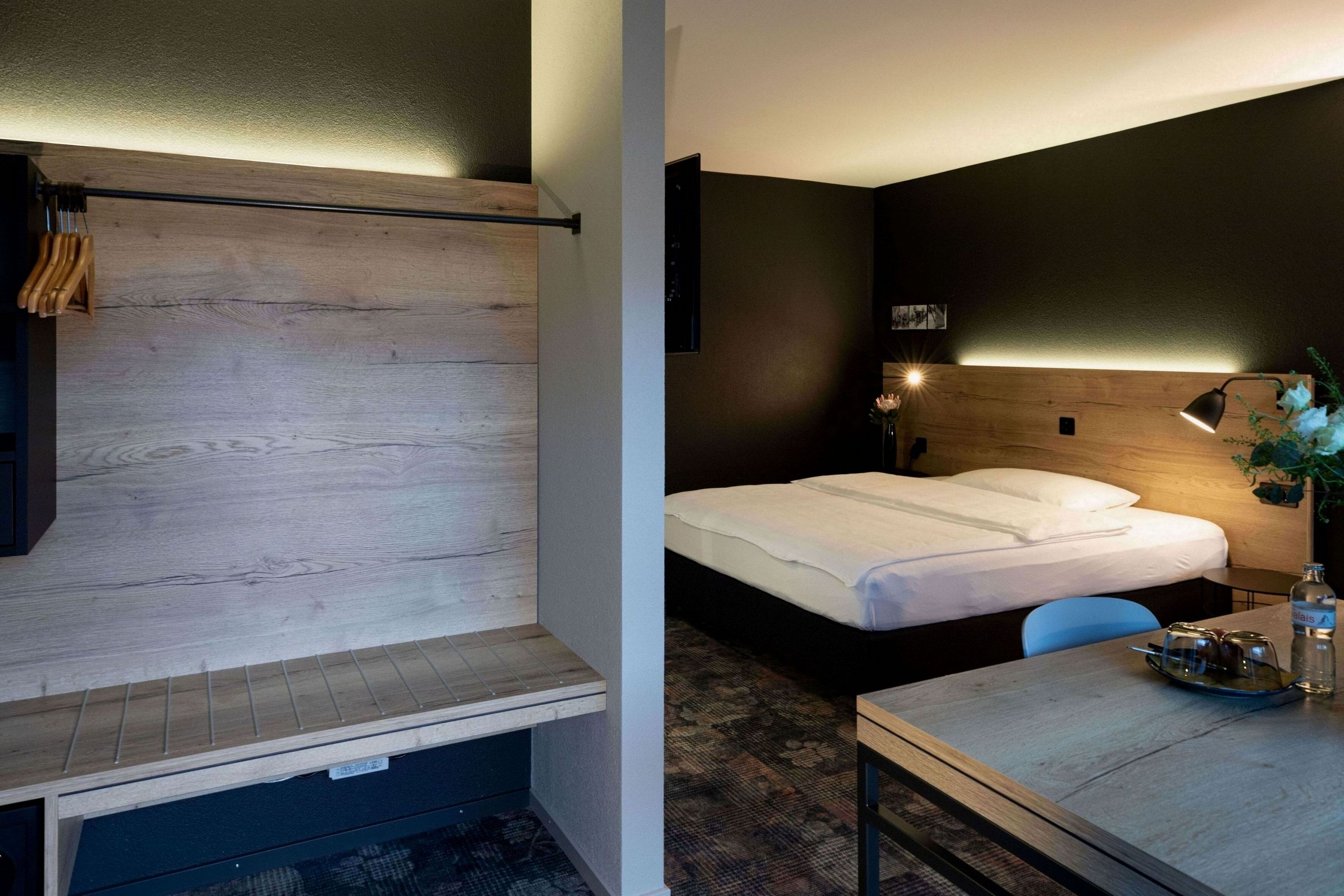 Une chambre d’hôtel comprenant un lit, un bureau, une chaise, une table de chevet, une lampe et un téléviseur fixé au mur.