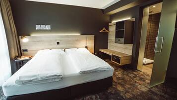 A modern hotel room with a large bed, a desk, a chair, a hanging light, and a mirror.