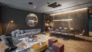 A modern lounge area with a sofa, round coffee table, and a dining table with chairs. - Baxter Hotel (Visp)