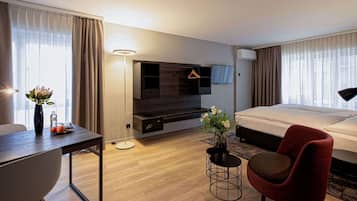 A hotel room with a bed, a desk, a chair, a TV, and a small table with a vase.