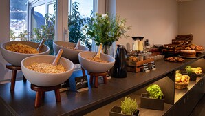 A buffet with various food items and a view of a mountainous landscape through a large window. - Baxter Hotel (Visp)