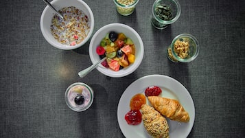 A breakfast setting with bowls of cereal, fruit salad, and pastries on a dark table.