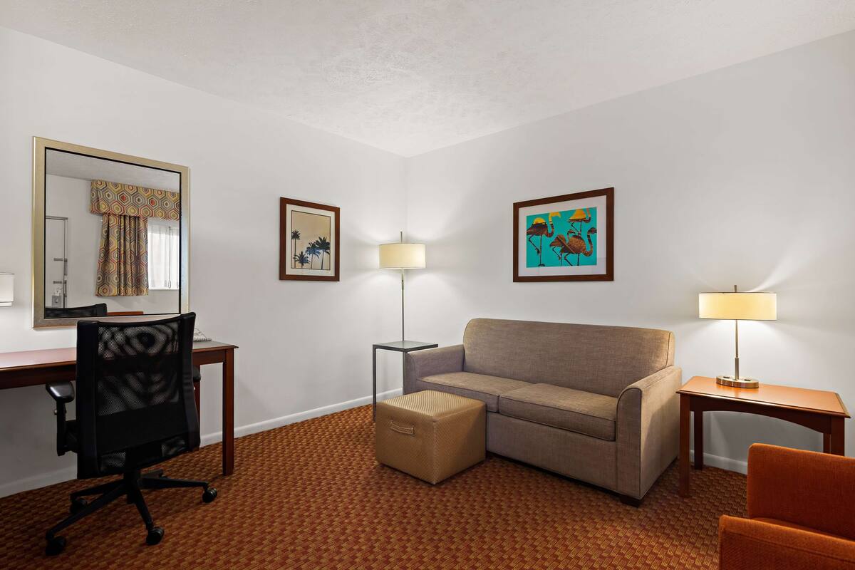 Une chambre d’hôtel équipée d’un bureau, d’un canapé, d’un petit pouf et de deux lampes.