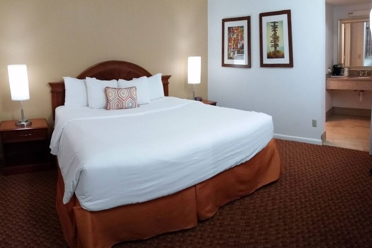 Une chambre d’hôtel avec un grand lit, deux tables de chevet, une commode, une coiffeuse et deux tableaux encadrés au mur.