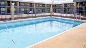 A motel with a swimming pool, a fenced parking area, and a building with multiple balconies.