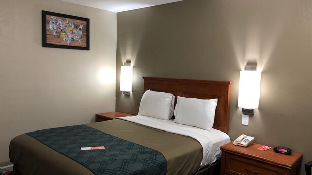 A hotel room with a bed, bedside tables, a nightstand, a telephone, and a wall-mounted light fixture.