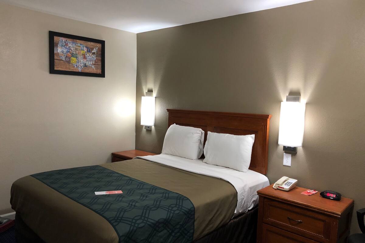 A hotel room with a bed, bedside tables, a nightstand, a telephone, and a wall-mounted light fixture.