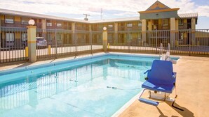 A swimming pool with blue chairs, a fenced area, and a building with balconies in the background.