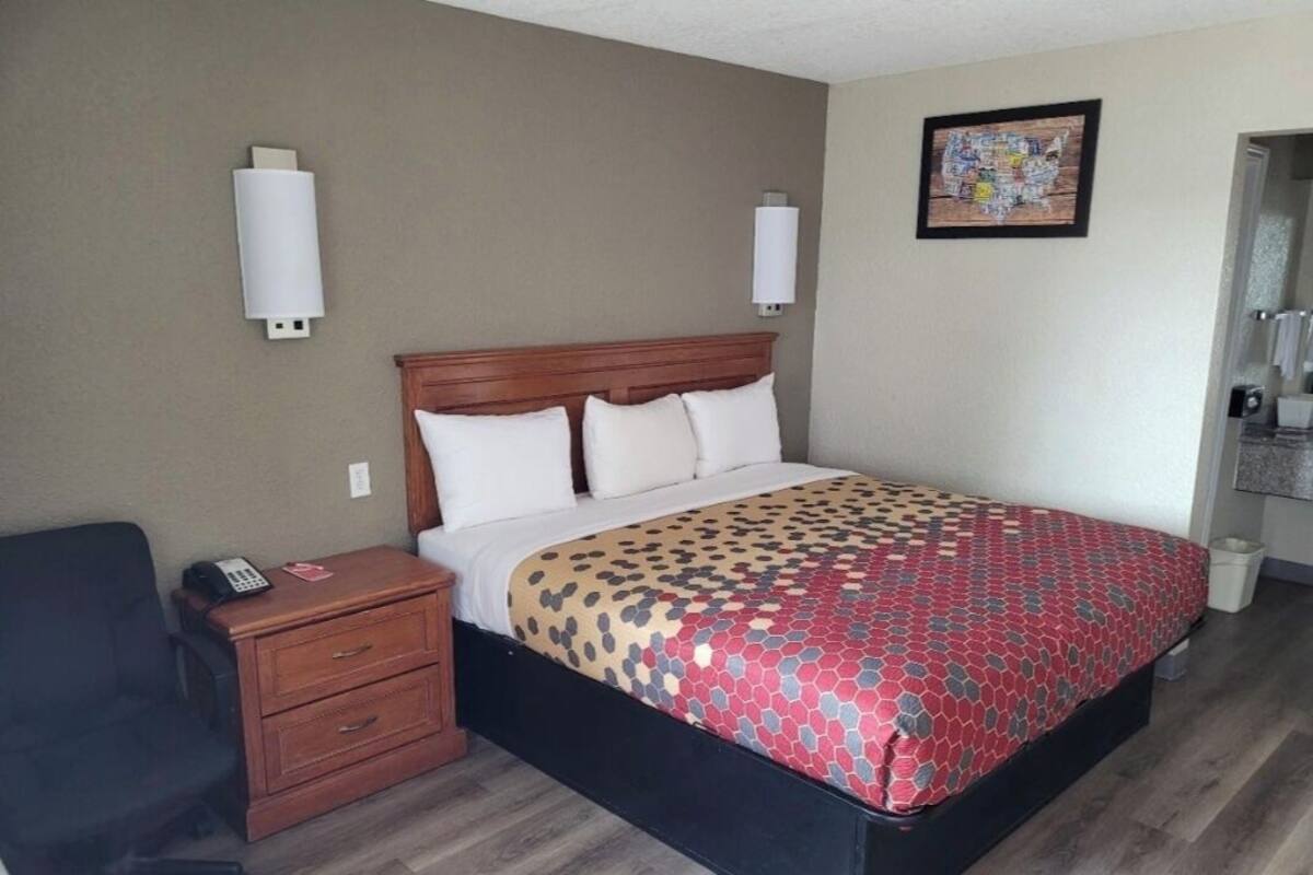 A hotel room with a bed, bedside table, and a chair.