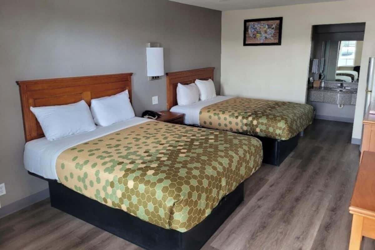 A hotel room with two beds, a small desk, a nightstand, a mirror, and a bathroom visible through an open door.