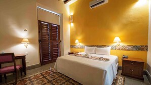 A hotel room with a bed, two bedside lamps, a wooden nightstand, a chair, and a patterned rug. - Hotel Del Gobernador (Mérida)