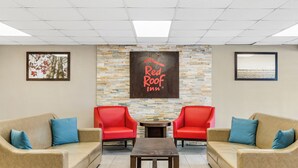 Un vestíbulo con dos sofás color beige, dos sillones rojos, una pequeña mesa de madera y una pared de piedra con el letrero de Red Roof Inn.